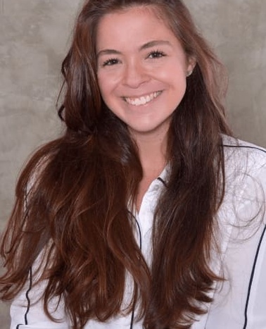 A young woman with long brown hair smiling in a white and black blouse.