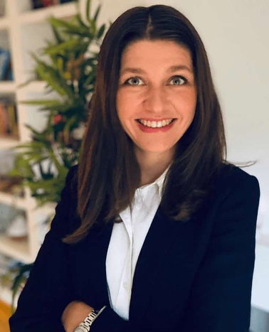 A professional woman smiling in an office setting surrounded by plants.