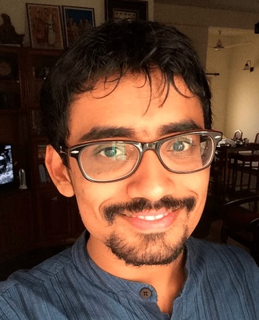 A portrait of a smiling man with glasses wearing a blue shirt.