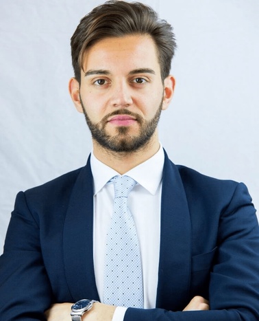 A professional portrait of a man in a blue suit and tie with a serious expression.