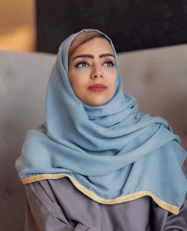 A woman in a blue hijab looks contemplatively to the side.