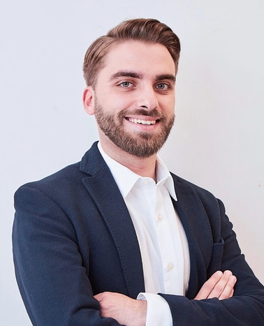A confident young man in a business suit smiling at the camera.