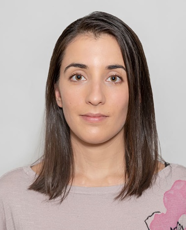 A portrait of a woman with medium-length brown hair wearing a light pink top with a pink graphic design.
