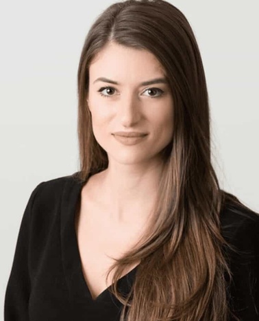 Portrait of a young woman with long brown hair wearing a black top, smiling gently at the camera.