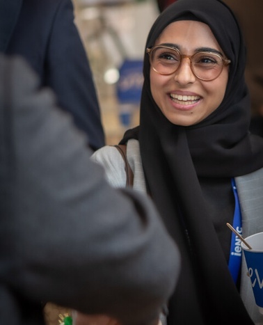A smiling woman in a hijab interacts with someone at an event.