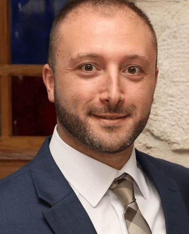 A portrait of a smiling man wearing a blue suit and striped tie.