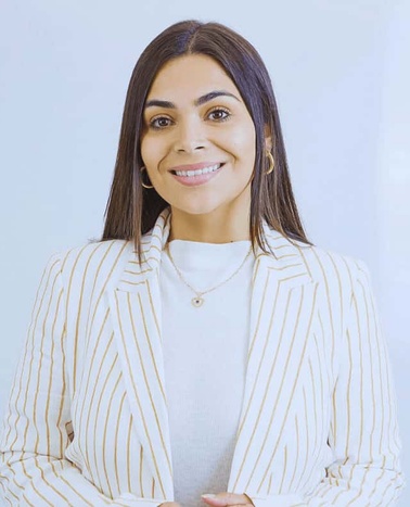 A smiling woman wearing a white striped blazer over a light gray top.