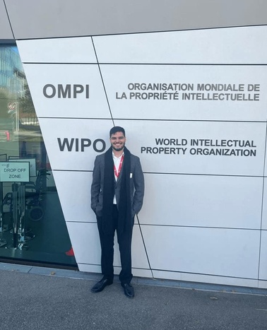 A man in a suit smiling at the camera, standing in front of the World Intellectual Property Organization (WIPO) building.