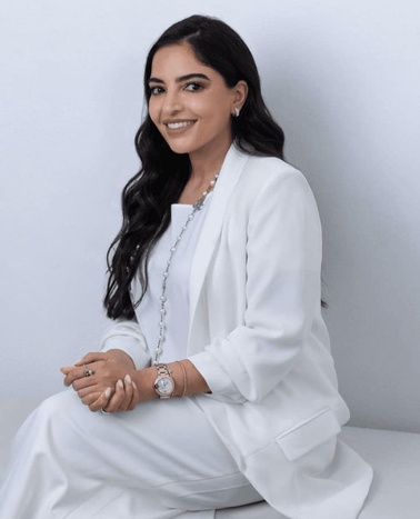 A woman in a white suit sitting with a smile.