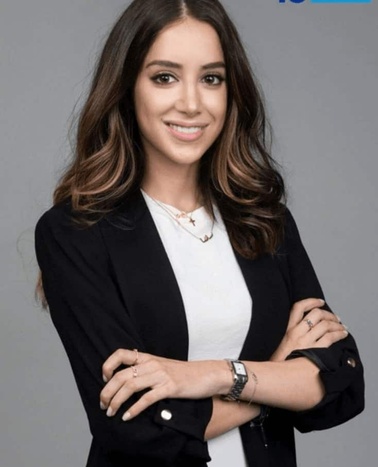 A professional portrait of a smiling woman wearing a black blazer over a white top, with crossed arms.