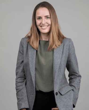A young woman smiling in a professional attire against a grey background