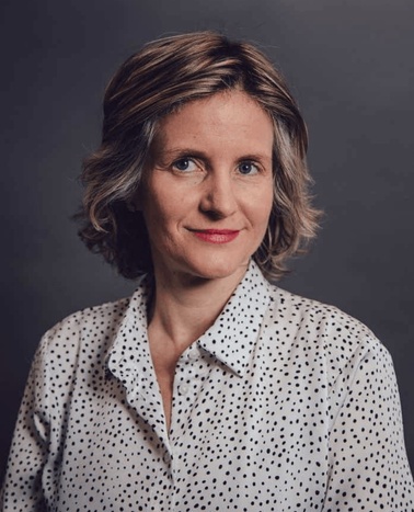 Portrait of a woman with short hair, wearing a polka dot shirt, against a dark background