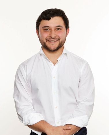 A young man with a beard and a friendly smile is posing for a professional portrait.