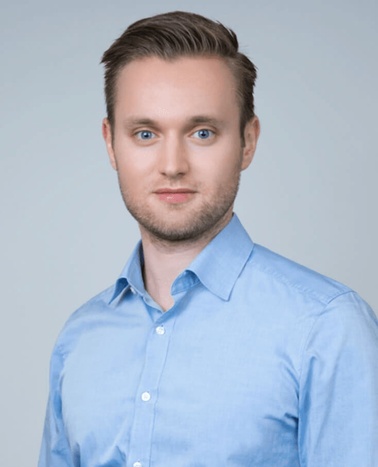 Portrait of a young man in a light blue shirt with short blond hair, looking at the camera.