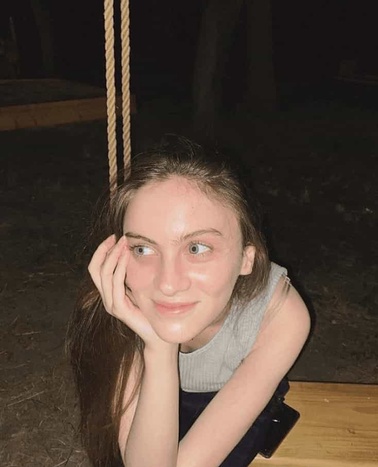 A young woman rests her chin on her hand while sitting on a swing at night.