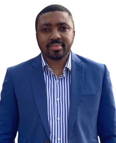 A man in a blue suit jacket and striped shirt stands against a white background.