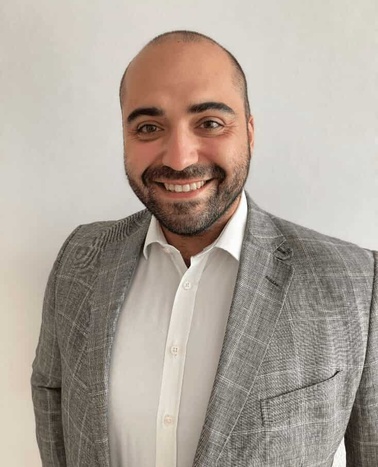 A man in a gray blazer and white shirt smiling at the camera.