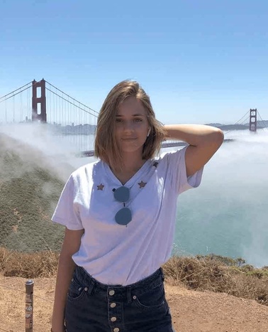 A woman standing in front of the Golden Gate Bridge partially obscured by fog.