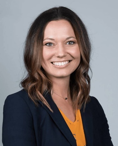 Portrait of a smiling woman with shoulder-length brown hair, wearing a navy blazer and an orange blouse.
