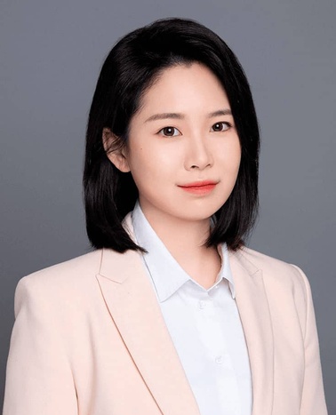 A professional headshot of a woman in a light pink blazer and white shirt.