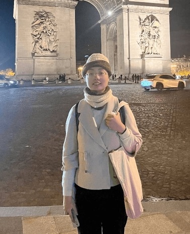 A person standing in front of the Arc de Triomphe at night.