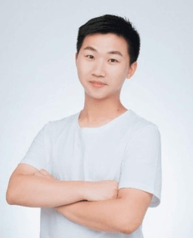 A young Asian man in a white t-shirt, standing with his arms crossed, smiling gently against a light gray background.