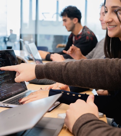 A group of students collaborating on a laptop in a classroom setting.