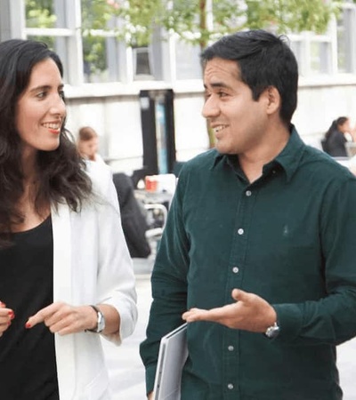 Two professionals, a man and a woman, are walking and talking animatedly in an outdoor urban setting.