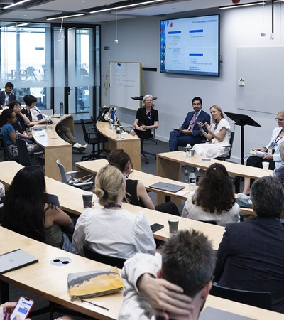 A group of people attending a presentation in a modern conference room with speakers at the front.