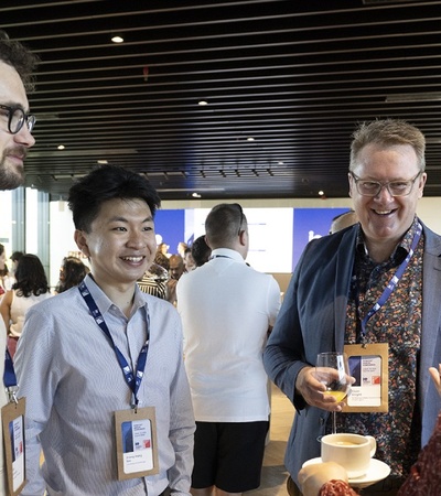 A group of people engaging in conversation at a networking event, holding coffee cups and wearing name tags.