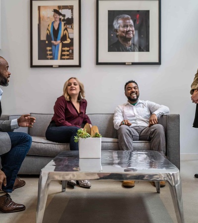 Four people, two men and two women, are having a lively conversation in a modern office lounge area.