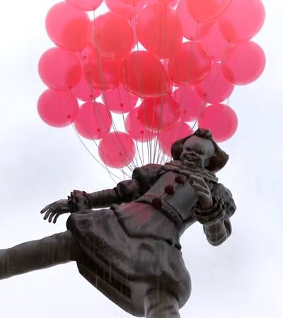 A whimsical statue of a clown holding a bunch of pink balloons.