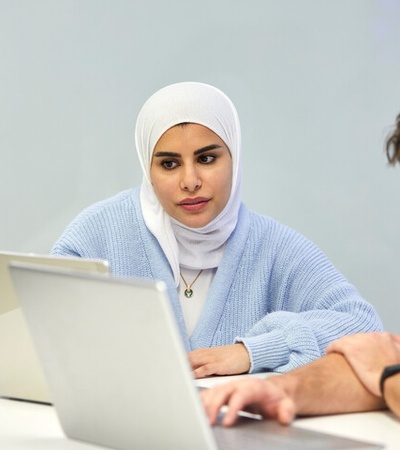 A woman in a hijab and a man are looking at a laptop screen in an office environment.