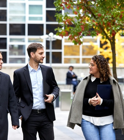 Three business professionals walking and talking outside a modern office building.