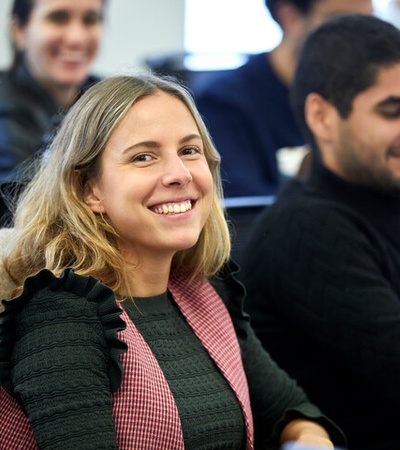 A smiling woman in a classroom setting surrounded by other students.