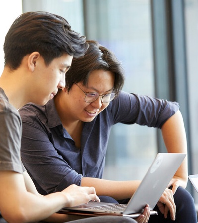 Two people are collaborating on a laptop while sitting together in a modern workspace.