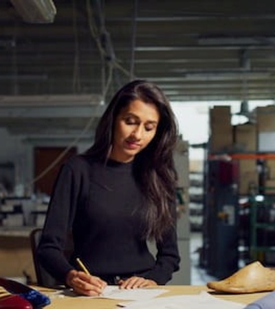 A woman working attentively at a drafting table in an industrial workspace filled with various design materials.