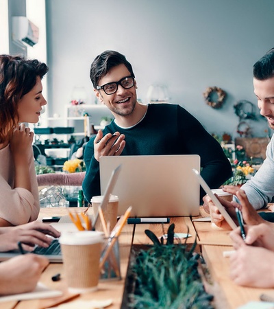 A group of young adults engaging in a collaborative discussion around a laptop in a brightly lit room.