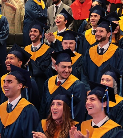 A group of young graduates in blue and yellow caps and gowns joyfully celebrating their graduation ceremony.