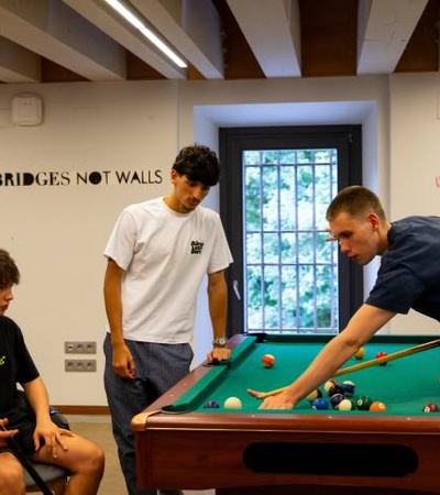 A group of four young men playing billiards in a cozy room with a motivational quote on the wall.