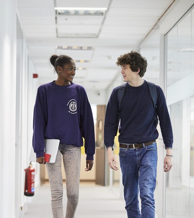 Two young people are walking together in a modern hallway.