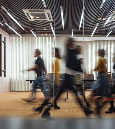 Blurry motion of busy people walking in a modern office corridor with wooden decor and glass partitions.