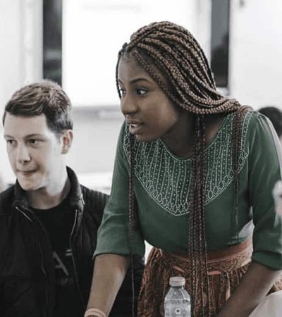 A woman in traditional attire engaging with a group of students in a classroom setting.