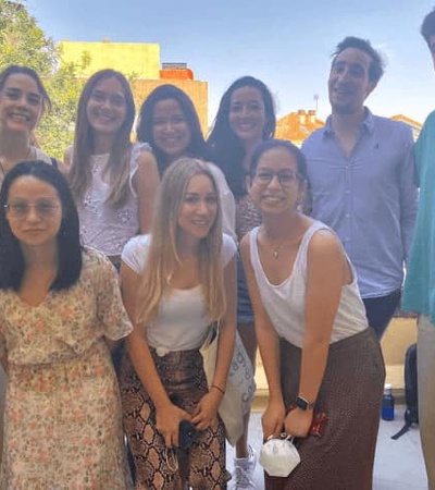 Group of ten young adults smiling on a balcony with a clear sky background.