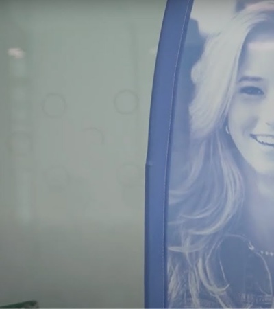 A woman working at a desk with a promotional poster of a smiling woman in the background.