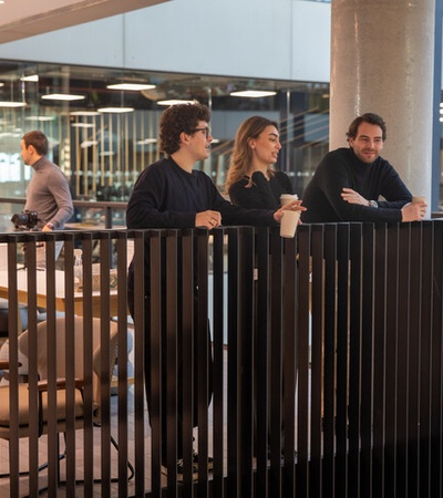 A group of three people stands on a balcony discussing in a modern office space.