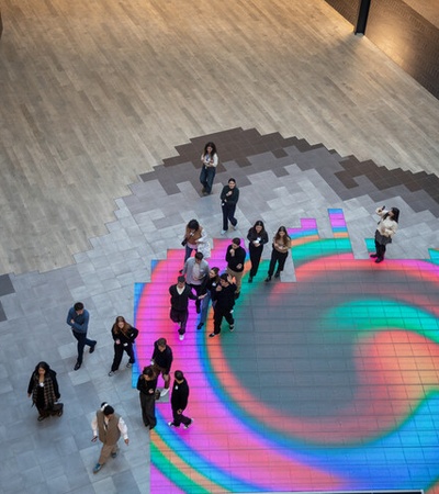 A group of people standing on a colorful, swirling light projection on the floor in a spacious indoor area.