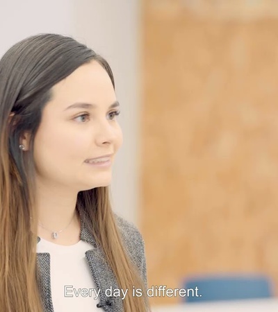 A woman with long hair speaks with a thoughtful expression in a modern office environment.