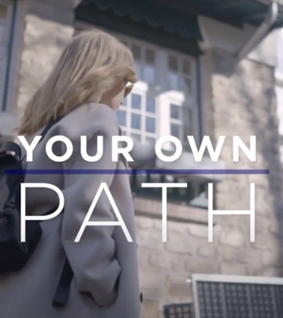 A woman walking past a building with the text 'YOUR OWN PATH' superimposed on the image.