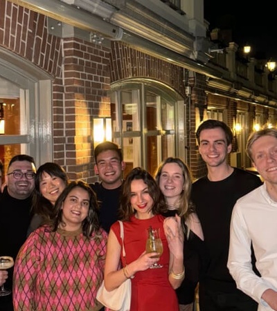 A group of nine people posing with drinks outside a brick building at night.